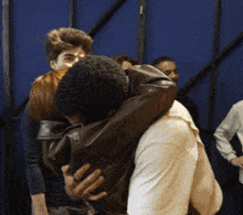 a man in a brown jacket is hugging another man in a white shirt