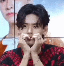 a young man is making a heart shape with his hands while sitting in front of a screen .
