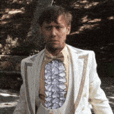 a man in a white suit has a ruffled vest