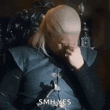 a man with blonde hair is sitting in a chair and rubbing his eyes .