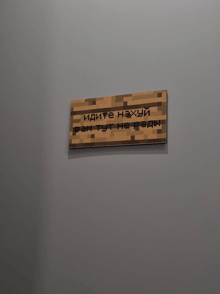 a wooden sign that says " идите нахуй " is on a gray wall