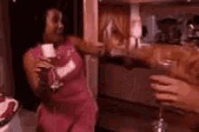 a woman in a pink dress is holding a glass of wine while standing next to another woman .