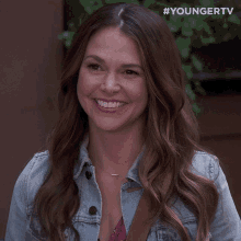 a woman in a denim jacket is smiling and waving at the camera