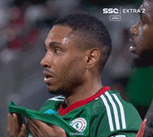 a soccer player wipes his face with a towel in front of a ssc extra 2 logo