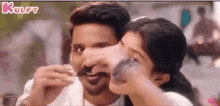 a man with a mustache is feeding a woman a spoon of food .