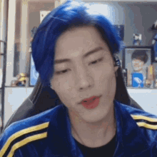 a man with blue hair is sitting in a chair with headphones on .