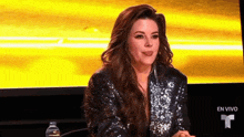 a woman in a sequined jacket is sitting in front of a yellow screen and making a funny face .