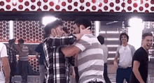 two men are hugging each other in front of a mirror in a room with other men .
