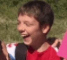 a young boy in a red shirt is smiling while holding a sign .