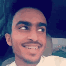 a young man with a mustache is smiling while sitting in a car .