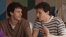 two young men are sitting at a table and talking