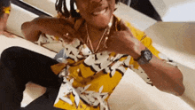 a man wearing a yellow shirt and a gold necklace is sitting on the floor .