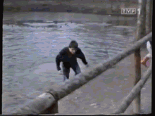 a man is jumping over a fence into a body of water with tvp in the corner
