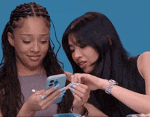 two women are looking at a phone together and one has long blue nails