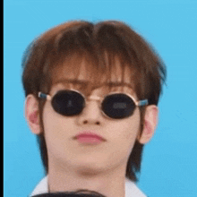 a young man wearing sunglasses and a white shirt is looking at the camera .
