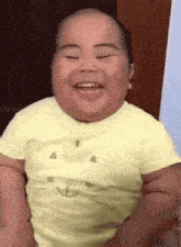 a baby wearing a yellow shirt with a smiley face on it is smiling