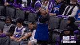 a woman in a blue kings jersey is sitting in the stands during a basketball game