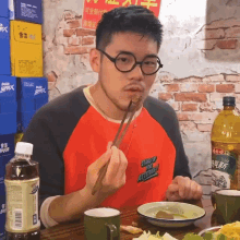 a man wearing a red shirt that says stand up for attitude is eating food with chopsticks
