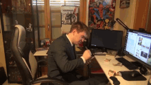 a man in a suit sits at a desk with a metal gear solid poster on the wall behind him