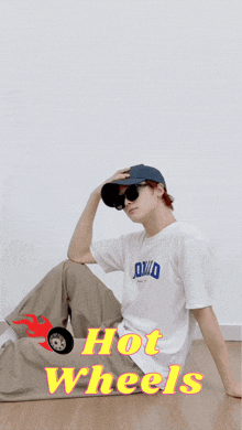 a person wearing a hat and sunglasses is sitting on the floor with the words hot wheels written above them