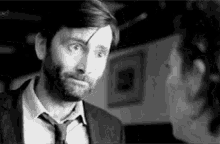 a man with a beard and tie is looking at a woman in a black and white photo .