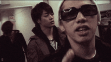 a man wearing sunglasses is standing next to another man in a hallway