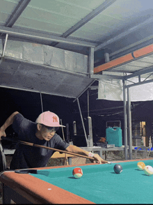 a man playing pool wearing a pink ny hat