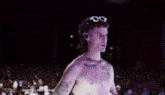 a man without a shirt is standing in front of a crowd wearing sunglasses .
