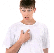 a young man wearing a white t-shirt is pointing at his chest .