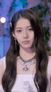 a woman wearing a necklace and earrings looks at the camera .