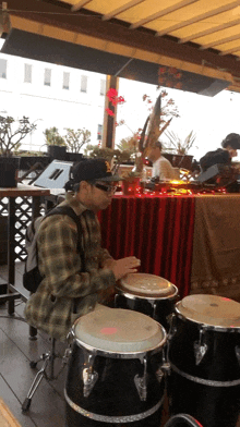 a man in a plaid shirt is playing drums in a room