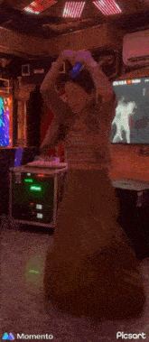 a woman in a long skirt is dancing in a room with a momento logo on the bottom left