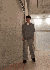 a man wearing a grey jacket and pants is standing in a hallway