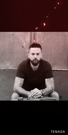 a man with a beard is sitting in front of a red wall with the word tenada on the bottom