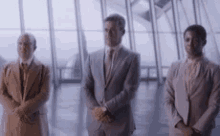three men in suits are standing next to each other in front of a large window .