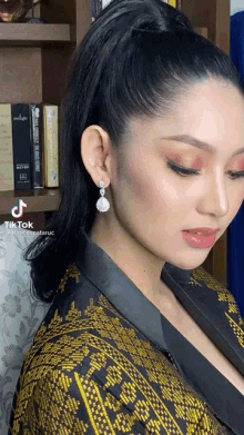 a woman wearing a ponytail and earrings is standing in front of a bookshelf with twilight books on it .