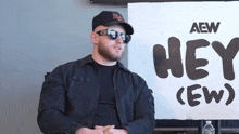 a man wearing sunglasses sits in front of a sign that says hey