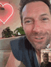 a man is smiling in front of a heart shaped neon sign