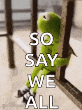 kermit the frog is sitting on a railing holding onto a railing .