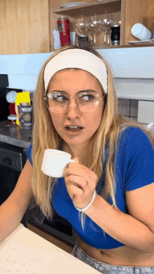 a woman wearing glasses and a headband is drinking from a cup