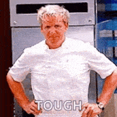 a man in a chef 's uniform is standing with his hands on his hips and says `` tough '' .