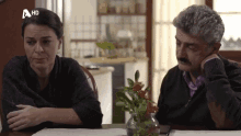 a man and a woman sit at a table with a hd logo on the bottom right