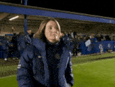 a woman in a nike jacket stands on a soccer field at night