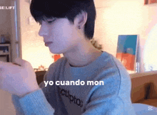 a young man is sitting at a table in a living room with a sweater that says yo cuando mon .