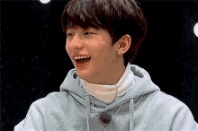 a young man wearing a hoodie and a white turtleneck is laughing with his mouth open .