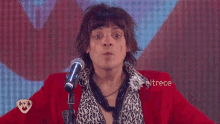a man in a red jacket stands in front of a microphone with eltrece written on the bottom