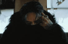 a man with a tattoo on his arm is covering his face with a black fur coat
