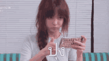 a woman is sitting on a couch looking at her cell phone with a foreign language written on it