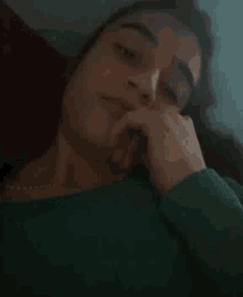 a woman in a green sweater is smiling with her hand on her face