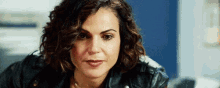 a woman with curly hair is wearing a leather jacket and a necklace .